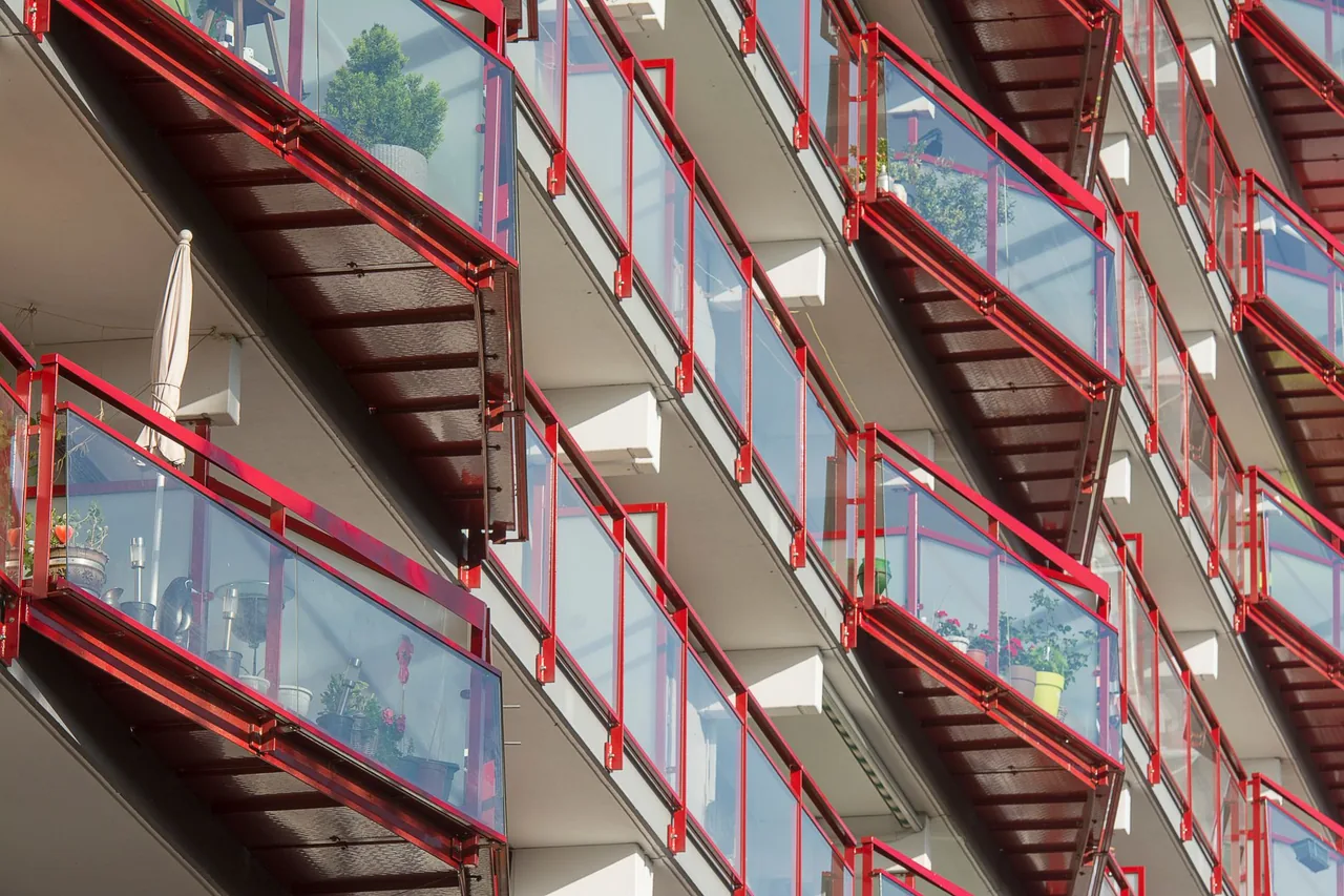 Elewacja bloku z rzędem balkonów na wspornikowych płytach, z donicami i roślinami za szklanymi balustradami